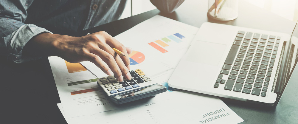 A man working about financial and analysis business document with calculator and holding glasses at his office to calculating expenses, Accounting concept